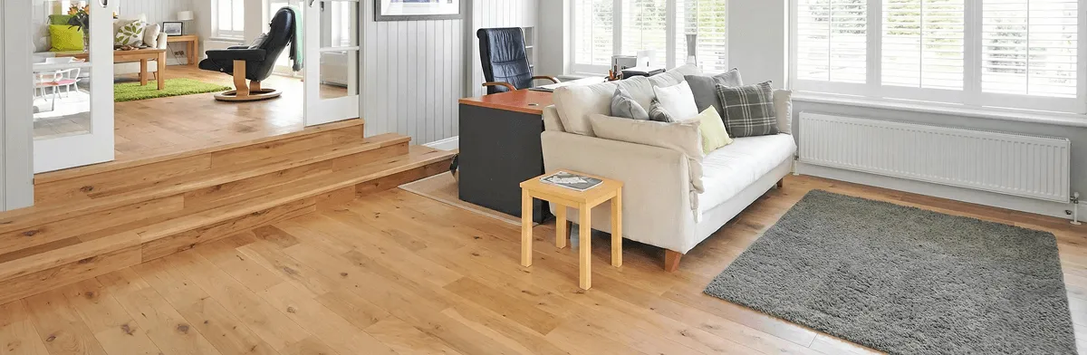 A modern living room with professionally installed laminate flooring, a beige sofa, a small side table, a gray rug, and large windows with white shutters in Dayton, OH